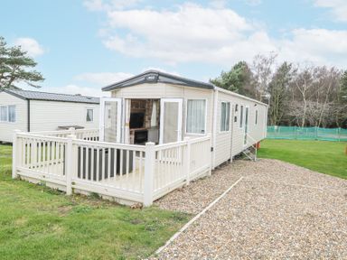 A static caravan with an open patio door and railing on a gravel driveway surrounded by grass at 75 Foxburrow Hang in Fritton