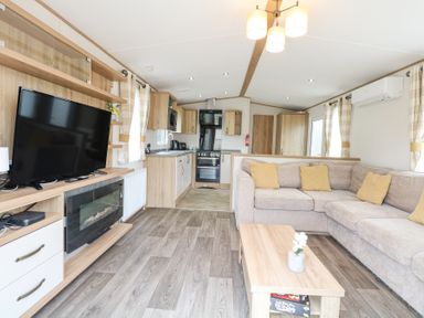 A living room with a sectional sofa and a coffee table next to a kitchen area at 75 Foxburrow Hang in Fritton