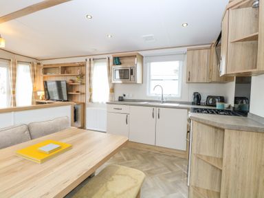 A kitchen and dining area with wooden cabinets a dining table and a television in a living space at 75 Foxburrow Hang in Fritton