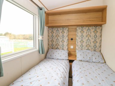 A bedroom with two single beds and a window with curtains at 75 Foxburrow Hang in Fritton