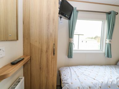 A bedroom with a bed near a window with curtains a wooden wardrobe and a small wall-mounted television at 75 Foxburrow Hang in Fritton