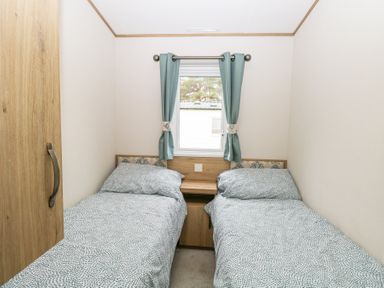 A bedroom with two single beds a window with curtains and a wooden cabinet at 75 Foxburrow Hang in Fritton