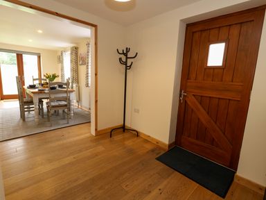 An entryway with a wooden front door and a coat rack next to an open dining room with a table and chairs at Little Dairy House near Swanage