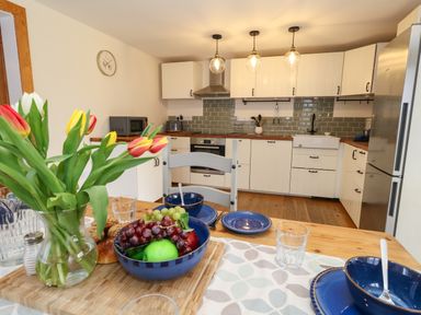 A kitchen with white cabinets wooden countertops pendant lights and a dining table set with blue dishes and a vase of tulips at Little Dairy House near Swanage