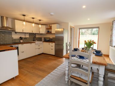 A kitchen with white cabinets a wooden dining table set with blue dishes and flowers at Little Dairy House near Swanage