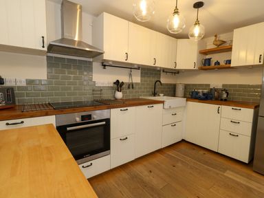 A kitchen with white cabinets wooden countertops green tiled backsplash and wooden floor at Little Dairy House near Swanage