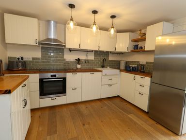 A kitchen with white cabinets wooden countertops a stainless steel oven and fridge green tiled backsplash and pendant lights at Little Dairy House near Swanage