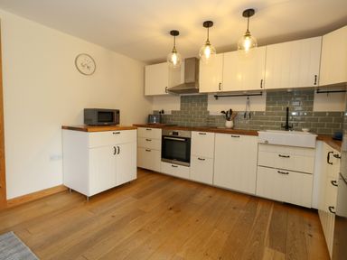 A kitchen with white cabinets wooden countertops and green tile backsplash at Little Dairy House near Swanage