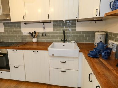 A kitchen with white cabinets wooden countertops a white sink and blue teapots and cups at Little Dairy House near Swanage