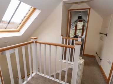 A carpeted staircase landing with white and wood banisters a skylight window and a doorway leading to a bedroom at Little Dairy House near Swanage