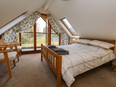 A bedroom with a wooden bed and two chairs near large windows at Little Dairy House near Swanage