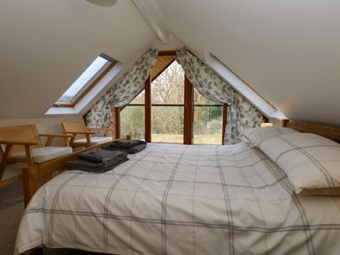 A bedroom with a bed two chairs and a large triangular window at Little Dairy House near Swanage
