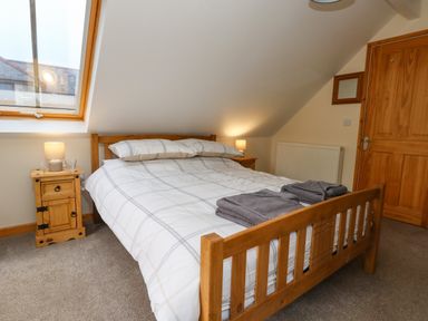 A bedroom with a wooden bed frame white and gray checked bedding two bedside tables with lamps and folded towels on the bed at Little Dairy House near Swanage