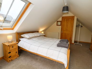 A bedroom with a wooden bed and side tables under a sloped ceiling with a skylight at Little Dairy House near Swanage