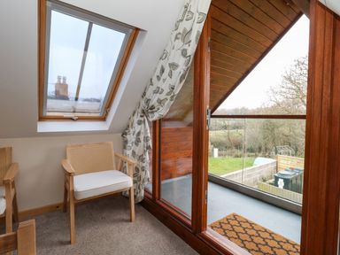A small seating area with two wooden chairs and a balcony with glass doors at Little Dairy House near Swanage