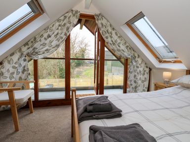 A bedroom with a bed and folded towels near skylight windows and a glass door leading to a balcony at Little Dairy House near Swanage