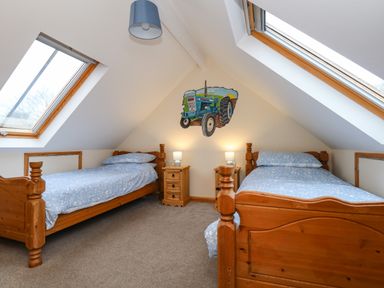 A bedroom with two wooden beds with blue bedding two bedside tables with lamps and skylight windows at Little Dairy House near Swanage
