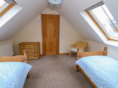 A bedroom with two single beds a wooden chest of drawers a wooden chair and skylight windows at Little Dairy House near Swanage