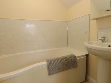 A bathroom with a bathtub a towel on the tub and a sink near Little Dairy House near Swanage