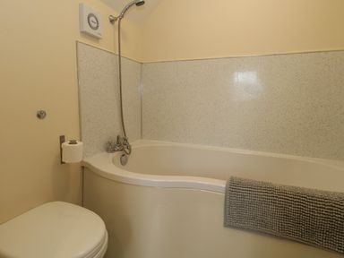 A bathroom with a bathtub shower combination a toilet and a towel on the bathtub edge at Little Dairy House near Swanage
