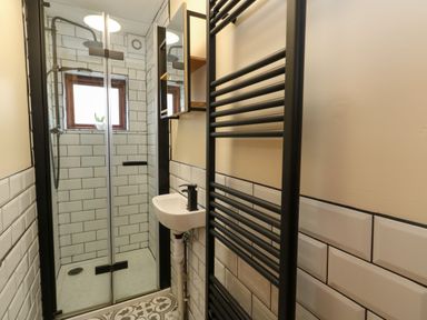A bathroom with a shower enclosure a small sink a black towel radiator and tiled walls at Little Dairy House near Swanage