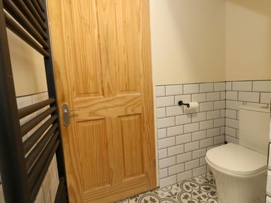 A bathroom with a wooden door a white toilet patterned floor tiles and white tiled walls at Little Dairy House near Swanage