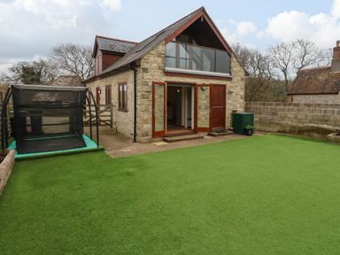 A stone house with open wooden doors and artificial grass in the yard at Little Dairy House near Swanage