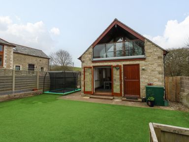 A backyard with artificial grass trampoline and stone house with wooden doors at Little Dairy House near Swanage