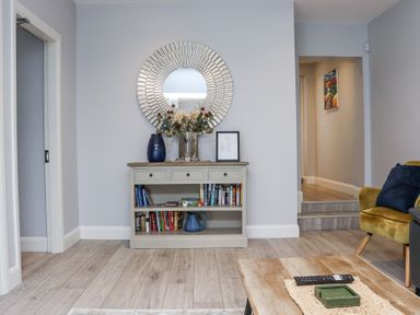 A room with a wooden floor a console table with books vases flowers and a round mirror above Daly's Place Ballyporeen County Tipperary