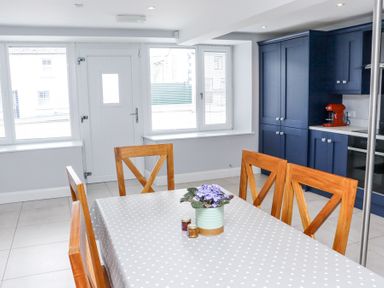 A kitchen with blue cabinets a dining table with wooden chairs and a plant in a pot at Daly's Place in Ballyporeen County Tipperary