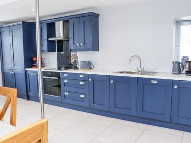 A kitchen with blue cabinets white countertop a stainless steel oven and sink at Dalys Place in Ballyporeen County Tipperary
