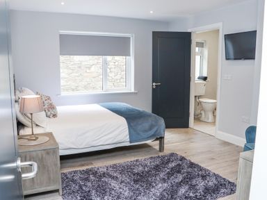 A bedroom with a bed a bedside table with a lamp a window and an open door leading to a bathroom at Daly's Place in Ballyporeen County Tipperary