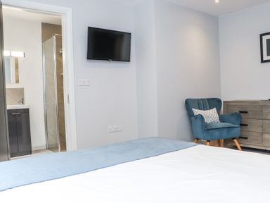 A bedroom with a bed a blue armchair a wooden dresser a wall-mounted television and an open door showing a bathroom at Dalys Place in Ballyporeen County Tipperary