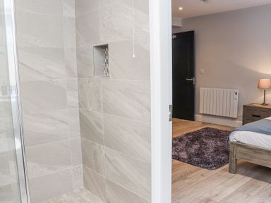 A bathroom with tiled shower next to a bedroom with a rug lamp and wooden furniture at Daly's Place in Ballyporeen County Tipperary