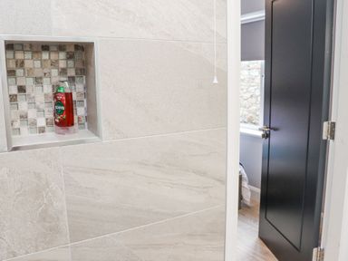 A tiled bathroom wall with a built in shelf holding a red bottle and an open door leading to a room with a bed at Dalys Place Ballyporeen County Tipperary