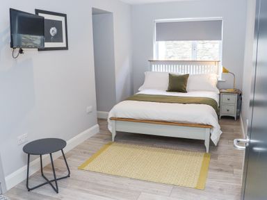 A bedroom with a bed a bedside table with lamp a small round table and a wall-mounted television at Daly's Place in Ballyporeen County Tipperary