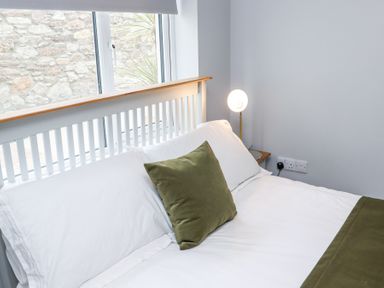 A bedroom with a white bed and green pillows by a window with a bedside lamp at Daly's Place in Ballyporeen County Tipperary