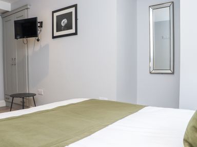 A bedroom with a bed covered in white and green bedding a wall-mounted TV a wardrobe a small round table a framed picture and a wall mirror at Daly's Place in Ballyporeen County Tipperary