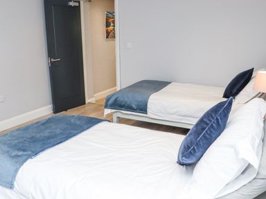 A bedroom with two single beds covered in white and blue bedding with a dark door on the left at Dalys Place in Ballyporeen County Tipperary