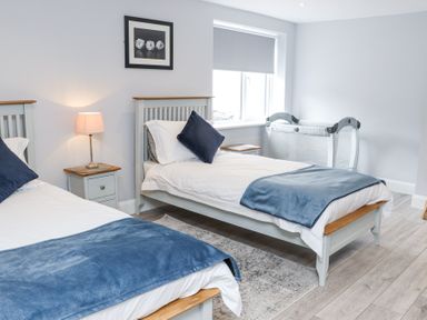 A bedroom with two single beds with blue blankets and pillows a nightstand with a lamp a window and a crib at Daly's Place in Ballyporeen County Tipperary