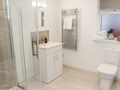 A bathroom with a shower enclosure a white vanity unit with a mirror a chrome towel radiator a toilet and a window with towels and a vase on the sill at Daly's Place in Ballyporeen County Tipperary