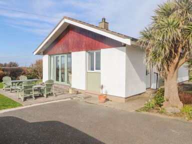 An exterior view of a single-story house with a small patio set and a tree at Seafield in Rhydwyn near Cemaes Bay