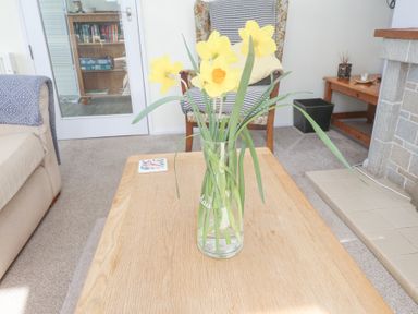A vase with yellow flowers on a wooden coffee table in a living room with a chair a sofa and a fireplace at Seafield in Rhydwyn near Cemaes Bay