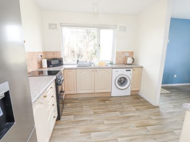 A kitchen with wooden cabinets a washing machine a black oven a microwave and a kettle at Seafield in Rhydwyn near Cemaes Bay