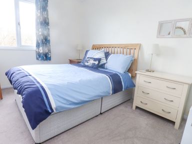A bedroom with a bed with blue bedding a wooden headboard a white dresser and two lamps at Seafield in Rhydwyn near Cemaes Bay