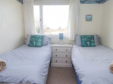 A bedroom with two single beds separated by a three-drawer white nightstand with a lamp on it at Seafield in Rhydwyn near Cemaes Bay