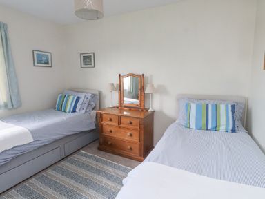 A bedroom with two single beds a wooden dresser with a mirror and two lamps a patterned rug and two framed pictures on the wall at Seafield in Rhydwyn near Cemaes Bay