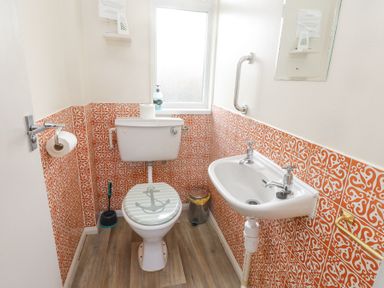 A small bathroom with a toilet, a sink, orange patterned tiles on the walls and a window at Seafield in Rhydwyn near Cemaes Bay