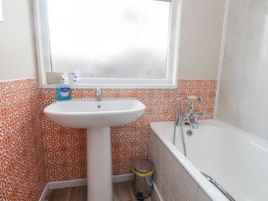 A bathroom with a white sink and bathtub with orange patterned tiles on the walls at Seafield in Rhydwyn near Cemaes Bay