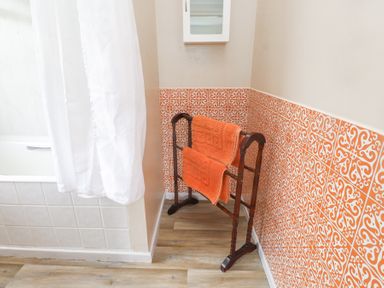 A bathroom corner with orange patterned tiles a wooden towel rack with orange towels and a white shower curtain at Seafield in Rhydwyn near Cemaes Bay